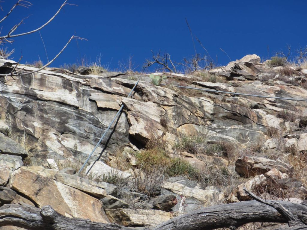 An image of two metal pipes, both about five feet long, coming out of a mottled grey and white rock cliff.